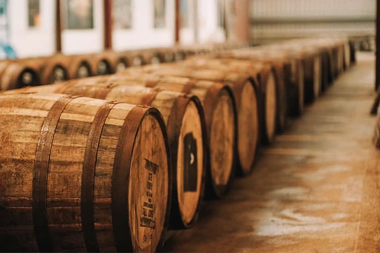 Barricas de whisky en una bodega, mostrando cómo la madera influye en el sabor del whisky según el tipo de madera y el tiempo de envejecimiento. La influencia de la madera en el whisky.