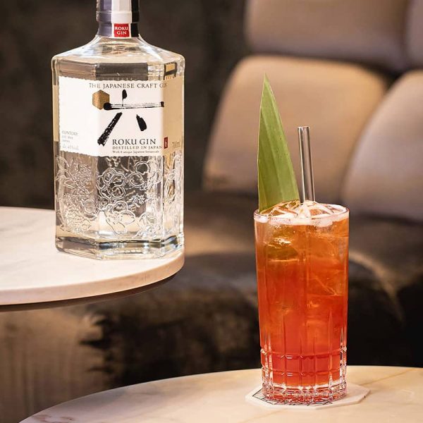 Botella de Roku Gin junto a un cóctel refrescante con rodajas de limón.